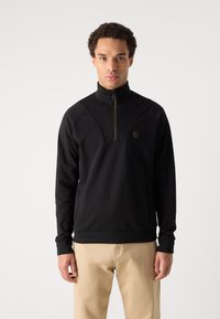 Felpa nera con zip, colletto alto, maniche raglan e un pannello decorativo sul petto. Presenta un logo e una texture liscia.