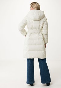 Cappotto bianco imbottito con cappuccio, vita con cintura e design trapuntato. Abbinato a jeans blu a zampa d'elefante e scarpe nere.