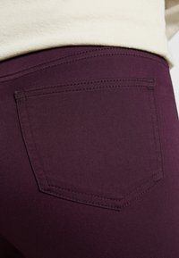 Pantalones de mezclilla morados con un bolsillo trasero. La tela tiene una textura suave y presenta costuras en contraste a lo largo del bolsillo y las costuras.