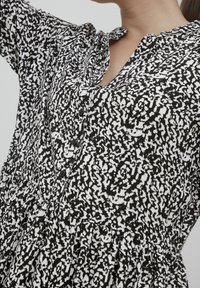 Musta-valkoinen kuviollinen paita napitetulla edellä, pehmeästä kankaasta ja rentoa istuvuutta, jossa on kerätty vyötärömuotoilu.