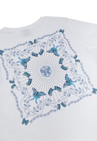Witte stoffen t-shirt met een centraal ontwerp van een blauwe vlinder, omringd door ingewikkelde bloemmotieven en stralende lijnen, textuur met subtiele details.