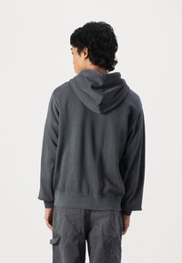 Dunkelgrauer Hoodie mit weicher Textur, ausgestattet mit einer Kängurutasche und verstellbarem Kordelzugkapuze. Etwas lockere Passform, schlichtes Design.