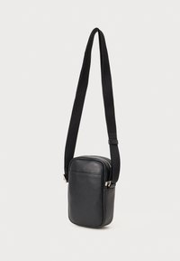 Borsa crossbody in pelle nera con chiusura a zip, forma rettangolare e tracolla in tessuto regolabile. Presenta una superficie testurizzata e hardware in argento.