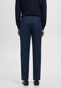 Spodnie w kolorze granatowym o prostym kroju, z dwoma tylnymi kieszeniami, szlufkami na pasek oraz subtelną fakturą; noszone z czarnymi butami.