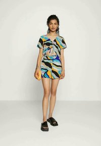 Conjunto curto colorido que apresenta uma blusa com mangas curtas e laço na frente, acompanhada de calções, feito de um tecido suave com padrões abstratos de ondas em azul, amarelo e preto.