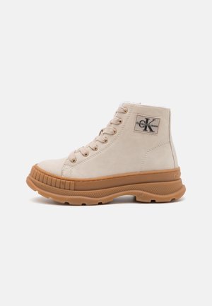 Sneaker alta in suede beige con suola in gomma marrone chunky, lacci e patch con logo Calvin Klein sulla caviglia.