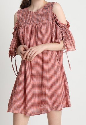 Frau trägt ein rot-weiß kariertes Cold-Shoulder-Kleid mit gerafftem Oberteil und Rüschenärmeln, die mit dünnen Bändern gebunden sind.