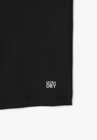 Närbild av svart tyg som visar en sydd fåll och liten vit text "ULTRA DRY" tryckt nära kanten.