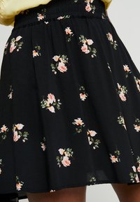 Schwarzer Rock mit elastischem Bund, mit einem floralen Muster in Pink und Weiß, gefertigt aus leichtem Stoff mit einer glatten Textur.