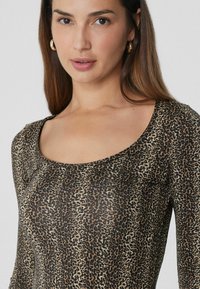 Dlouhý rukáv top v průhledné tkanině s leopardím vzorem, s kulatým výstřihem a přiléhavým siluetou. Barevná paleta zahrnuje béžovou a černou.