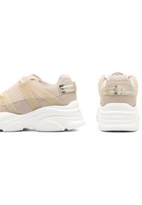 Zapatillas deportivas de color beige claro con paneles de malla y ante, suela de goma y detalles transparentes. Presentan un cuello acolchado y detalles metálicos.