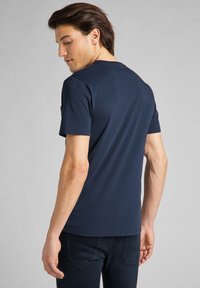 T-shirt in cotone blu navy con maniche corte, vestibilità slim, scollatura tonda e texture liscia. Mostrato di spalle, con un design semplice.
