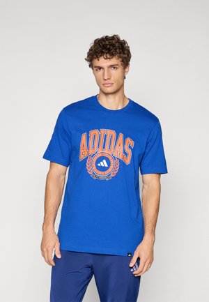 Mėlynas medvilninis marškinėliai su dideliu oranžiniu "ADIDAS" logotipu ir apvaliu emblema po juo. Trumpi rankovės ir apvalus kaklo iškirpimas.