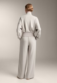 Ljust grå, oversized sweatshirt med hög krage och vida ärmar, ihop med matchande löst sittande byxor. Slät tygtextur.