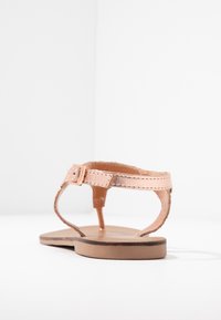 Leren teenslipper in lichtbeige met een flat sole, verstelbare enkelband en minimalistisch ontwerp met subtiele stikdetails.