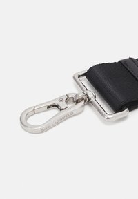 Czarna tkanina pasek z metalowym zapięciem i klamrą w kolorze srebrnym. Zapięcie posiada wygrawerowaną nazwę marki. Tekstura jest gładka z delikatnym połyskiem.