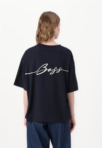 Navy oversized t-shirt in cotton fabric with short sleeves. Features white "Boss" text in cursive on the back. Relaxed fit and crew neck.