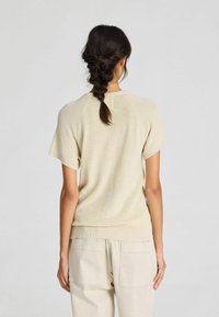 Light beige knitted sweater with short sleeves, ribbed hem, and crew neck design, paired with light beige straight-leg pants.