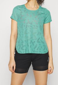 Lekka, turkusowa koszulka sportowa o teksturowanym, perforowanym wzorze. W zestawie z czarnymi szortami z siateczkową nakładką.