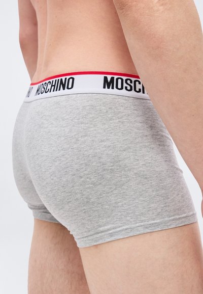 Άνδρας που φοράει ανοιχτό γκρι εσώρουχα boxer με λευκή ζώνη μέσης που φέρει μαύρο κείμενο "MOSCHINO" και μια κόκκινη ρίγα στο πάνω μέρος.
