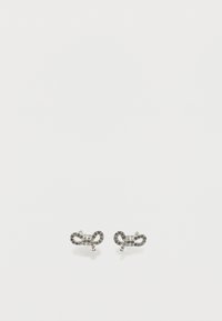 Μικρά ασημένια σκουλαρίκια σε σχήμα φιόγκου, διακοσμημένα με διάφανα και μαύρα στρας σε απλό λευκό φόντο.