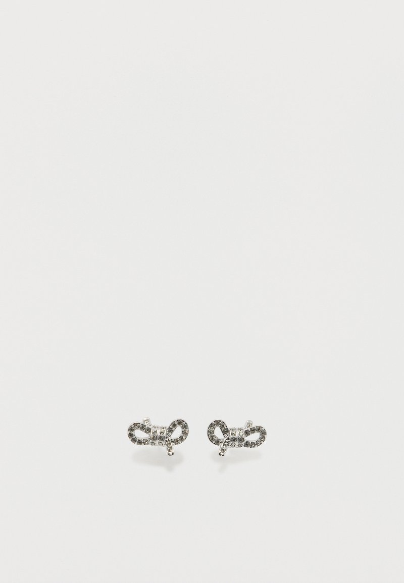 Μικρά ασημένια σκουλαρίκια σε σχήμα φιόγκου, διακοσμημένα με διάφανα και μαύρα στρας σε απλό λευκό φόντο.