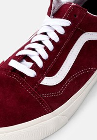 Røde suede sneakers med hvite snører, kontrasterende hvit sidestripe og gummisåle med teksturdetaljer.