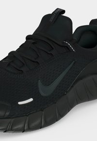 Μαύρο αθλητικό παπούτσι Nike με πλέγμα στο επάνω μέρος, κυματιστή υφή στη σόλα και ταινία έλξης με την ένδειξη «Nike Free» στη γλώσσα.