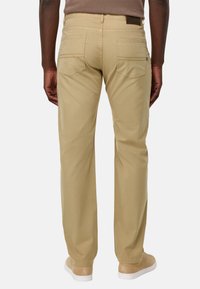 Pantalones de algodón beige con corte recto, bolsillos traseros visibles y detalles de costura sutiles, combinados con zapatillas de color claro.