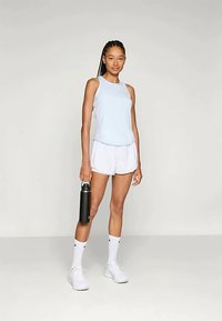 Gaiši zila bezpiedurkņu sporta krekls, balti šorti, balti zeķes un melni apavi. Tur melnu ūdens pudeli. Vienkāršs dizains, brīvs piegriezums.