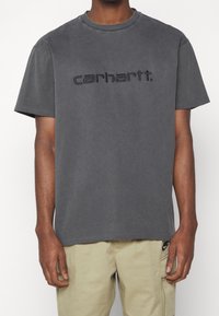 Grijze katoenen T-shirt met een ronde hals, met het reliëfmerklogo "carhartt" gecentreerd op de voorkant. Casual pasvorm en korte mouwen.