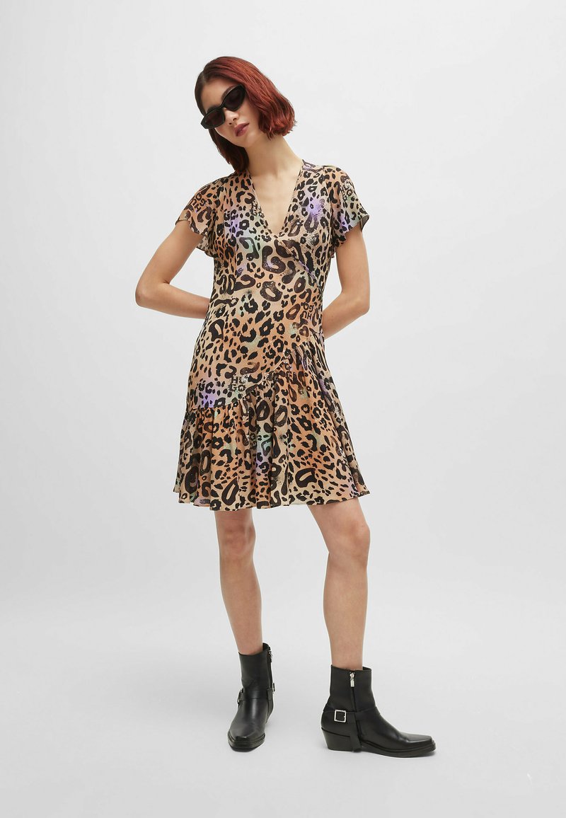 Leopard print dress in sheer material with a flared hem. Features short sleeves and a deep V neckline. Paired with black ankle boots.