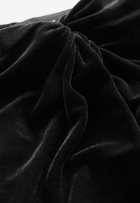 Tissu en velours noir avec une texture douce et lisse, comportant un détail froncé au centre, créant des vagues et des plis dans tout le matériau.