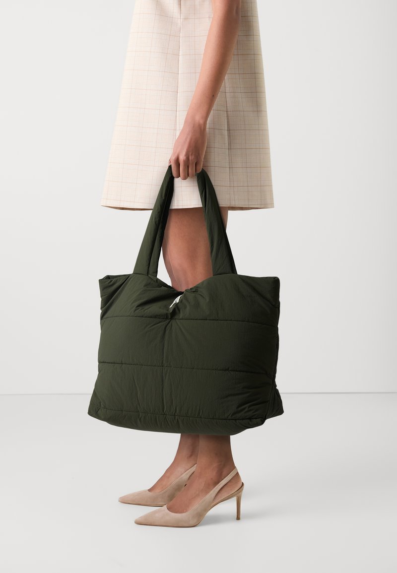 Sac fourre-tout vert rembourré avec fermeture éclair, doté de deux poignées robustes et d'une forme rectangulaire. Matériau en nylon texturé avec un design matelass�é.