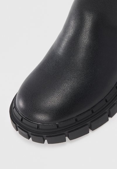 Svart ankelboot med texturerat läderöverdrag, rund tå och robust gummisula med djupa mönster för bättre grepp.
