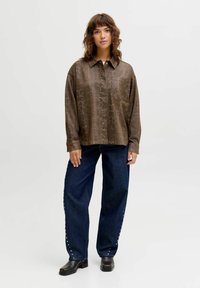 Gaiši brūna krekla ar čūskas raksta apdruku, pārizmēra piegriezums ar vienu krūšu kabatu; kombinēts ar tumši zilām, platām džinsa biksēm ar pērļu līdzīgiem akcentiem.