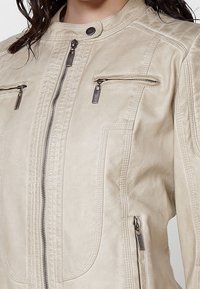 Kremowa skórzana kurtka z przednim suwakiem, ozdobnymi szwami i dwiema zapinanymi na zamek kieszeniami na piersiach. Gładka faktura z akcentami srebrnego metalu.