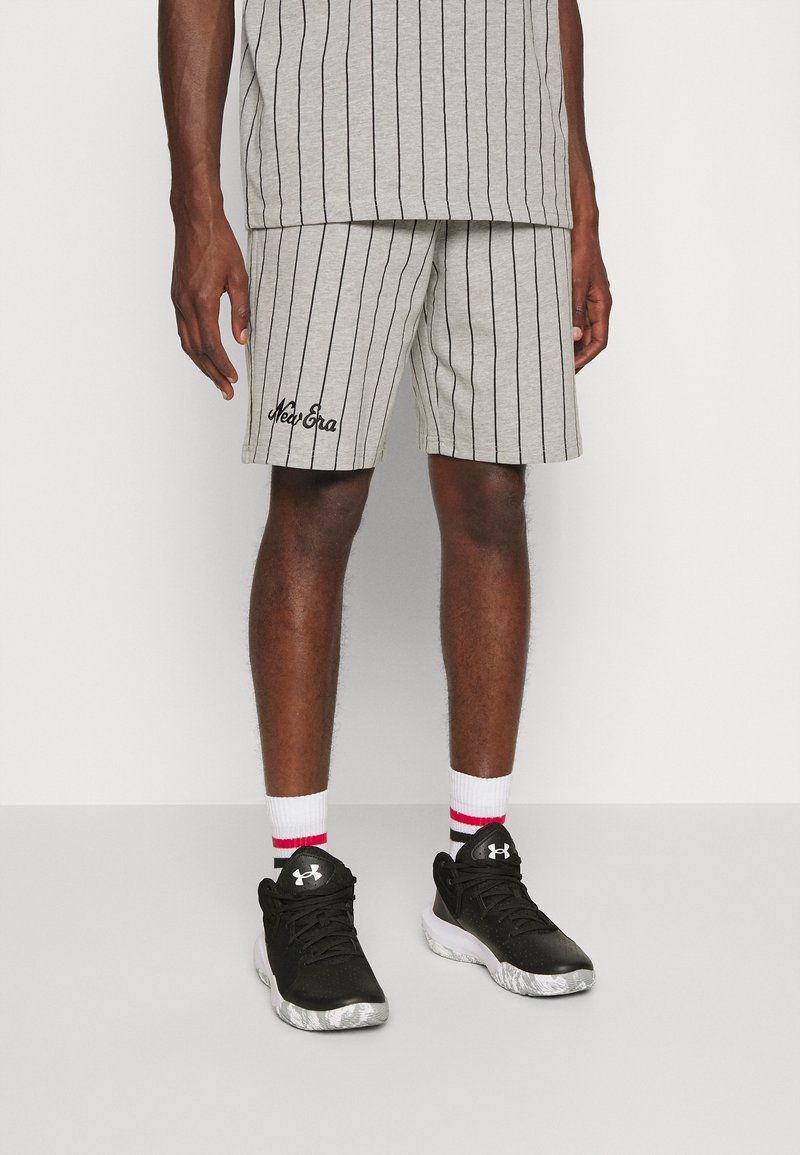 Grårandiga shorts med svart broderi, kombinerade med svarta joggingskor och vita strumpor med röda ränder. Enkel design, avslappnad stil.