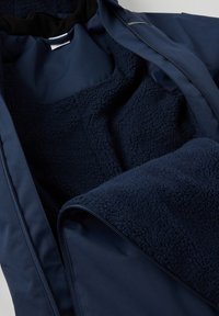 Marineblauwe jas met een zachte, gestructureerde fleece binnenvoering en een gladde buitenkant; heeft een rits en binnenzakken voor functionaliteit.