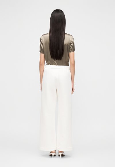 Top de cetim verde-oliva com mangas curtas, combinado com calças largas brancas. Textura suave, corte ajustado e comprimento curto na cintura.