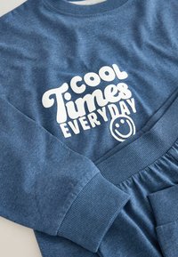 Blå sweatshirt med ribbede manchetter, der har hvid tekst "Cool Times EVERYDAY" og et smilende ansigt. Blød, afslappet pasform og i en bomuldsblanding.