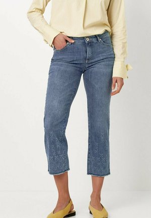 Hellblaue, taillierte Jeans mit einem dezenten floralen Stickmuster am Saum, ausgestattet mit einer schmalen Passform und ausgefransten Kanten. Dazu eine gelbe Bluse.