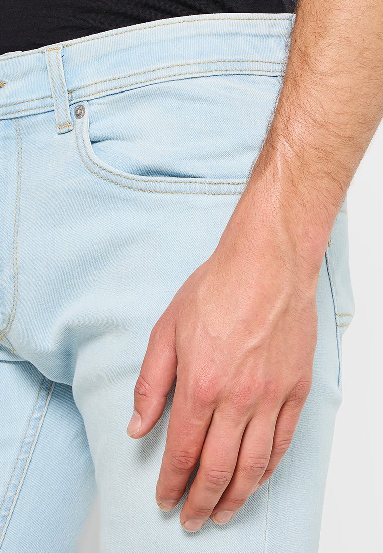 Helle blaue Denim-Jeans mit Slim-Fit, ausgestattet mit hellem Nähen, fünf Taschen und einem Knopfverschluss in der Nähe des Bundes.