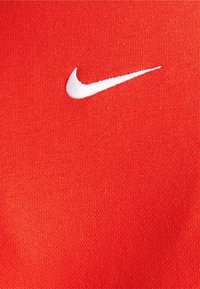 Tela roja con un prominente logo de Nike en forma de swoosh blanco. La textura es suave con un tejido apretado. El logo está bordado.