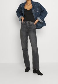 Mörkgrå högmidjade jeans med rak passform, tillsammans med en svart linne och en oversized blå denimjacka. Svarta ankbooties fulländar looken.