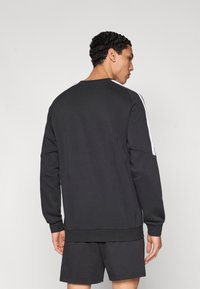 Μαύρο φούτερ με στρογγυλή λαιμόκοψη, μακριά μανίκια και λευκές ρίγες στο πλάι. Κατασκευασμένο από απαλό υλικό, με άνετη εφαρμογή και ριμπ μανσέτες.