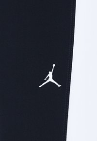 Juodi sportiniai kelnės su baltu Jumpman logotipu šone, pagamintos iš minkštos medžiagos su lygia tekstūra ir kontrastingomis siūlėmis.