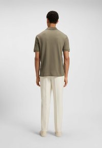 Polo shirt in olijfgroen, korte mouwen, geweven stof. Gecombineerd met crème gekleurde maatwerk broeken en lichtgekleurde instappers.