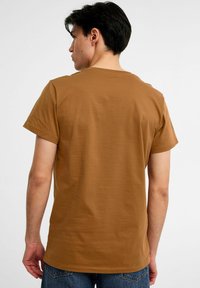 Brun bomulds T-shirt med rund hals og korte ærmer, der har et sømløst rygdesign og en afslappet pasform. Båret med blå jeans.