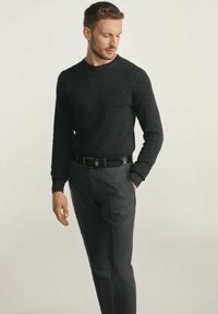 Czarny sweter z teksturowanego dzianiny o okrągłym dekolcie, zestawiony z dopasowanymi ciemnoszarymi spodniami oraz czarnym paskiem z prostokątną klamrą.